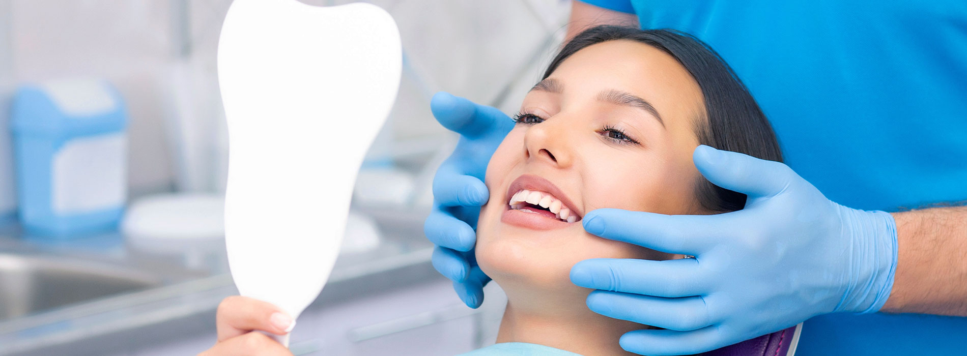 A person is seated in a dental chair, receiving care from a dental professional who stands behind them.