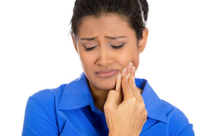 A woman in a blue shirt is intently looking at her hand, which she's holding up to her face.